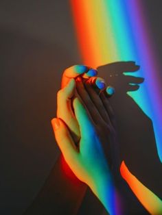 two hands holding each other in front of a rainbow light