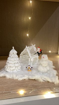 two snowmen and a house made out of toilet paper on a table with lights in the background