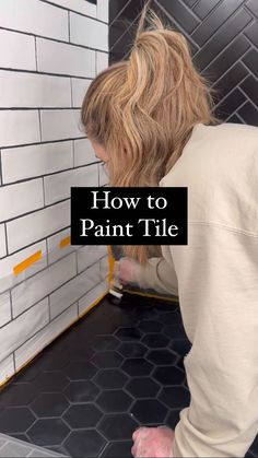 a woman in white shirt painting tile on wall with black and yellow lettering that reads how to paint tile