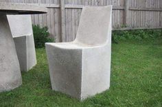 two cement chairs sitting in the grass next to a table