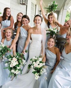 a group of women standing next to each other in front of a white house holding bouquets