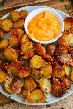 a white plate topped with fried potatoes covered in cheese and sauce next to a bowl of dip