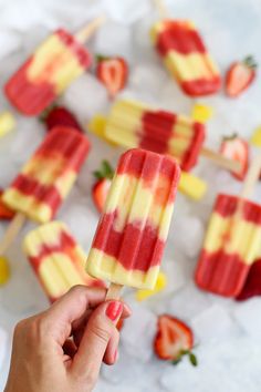 a hand holding a popsicle with strawberries on it and other popsicles in the background