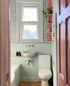 a white toilet sitting under a bathroom window next to a sink and bathtub in a bathroom