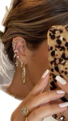 a woman is looking at her cell phone while wearing ear cuffs and leopard print earrings