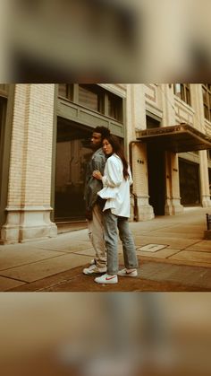 two people standing on the sidewalk in front of a building and looking at each other