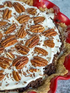 a pie topped with whipped cream and pecans in a red dish on a table