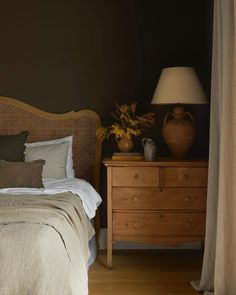 a bed sitting next to a wooden dresser with two vases on top of it