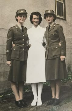 three women dressed in uniforms standing next to each other near a building with a window