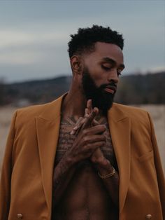 a man with tattoos on his chest wearing a yellow jacket and holding his hands together