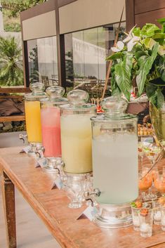 there are many drinks on the table with glasses next to each other and some plants