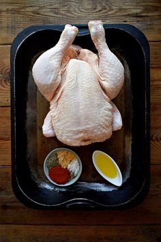 a raw chicken sitting on top of a pan next to two bowls of seasoning