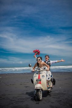 two people on a scooter with flowers in their hand and one person sitting on the back