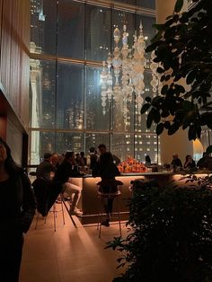 people are sitting at tables in front of large windows with city lights on the walls