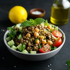 a white bowl filled with beans and cucumbers next to lemons, tomatoes, and oil