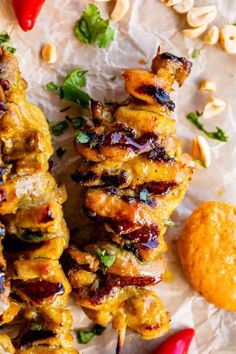 grilled chicken skewers with peanuts and cilantro on parchment paper next to red peppers