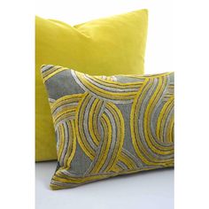 two yellow and grey decorative pillows on a white surface with one in the foreground