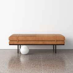 a brown bench sitting next to a white ball on top of a tiled floor in front of a wall