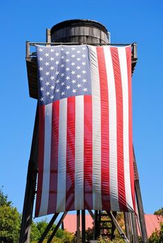 an american flag is hanging on the side of a water tower with trees in the background