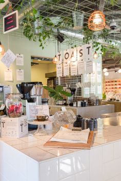 the inside of a coffee shop with plants hanging from the ceiling and menus on the counter