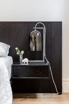 a nightstand with a lamp on top of it next to a night stand and flowers