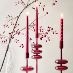 three red candles are lit in front of a vase with branches and berries on it