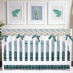 a white crib with blue and green bedding in front of two pictures on the wall