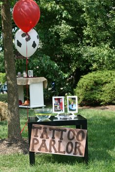 a table with a sign and balloons attached to it that says tattoo parlor on it