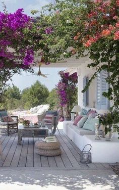 an outdoor living area with wicker furniture and flowers on the pergolated roof