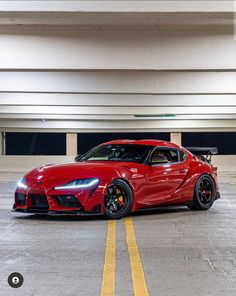 a red sports car is parked in a parking garage with yellow lines on the floor