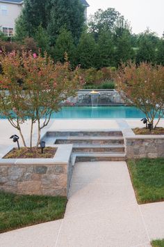 an outdoor swimming pool with steps leading to it and trees in the foreground, surrounded by landscaping