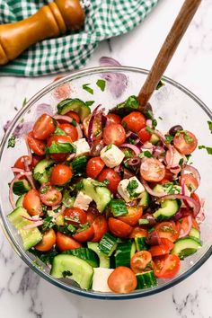 a glass bowl filled with cucumber, tomato and onion salad next to a wooden spoon