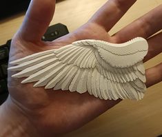 a person's hand holding a white paper angel wing