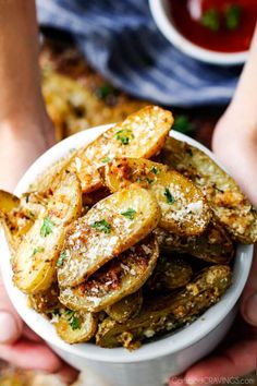 a person holding a bowl full of fried potatoes with parmesan cheese on top