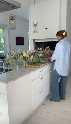 a woman is standing at the sink in her kitchen with flowers on the counter top