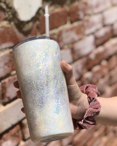 a person holding a glittered cup in front of a brick wall with a straw