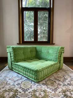 a green couch sitting in front of a window on top of a carpeted floor