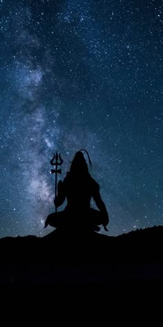 the silhouette of a person sitting on top of a hill under a night sky filled with stars