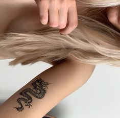 a woman with long blonde hair has a dragon tattoo on her arm and behind her head