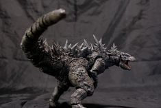 a godzilla action figure is posed in front of a black background with its mouth open