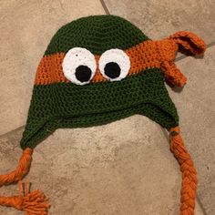 a crocheted hat with googly eyes on the front and sides, sitting on a tile floor