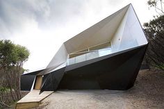 an unusual black and white house with stairs leading up to it's upper level