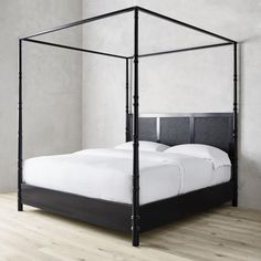 a black metal bed frame with white sheets and pillows on the bottom, in a room with light wood flooring