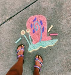 a person standing in front of a chalk drawing of a snail on the ground with crayons next to it