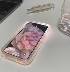 a cell phone sitting on top of a white table next to a glass and pen