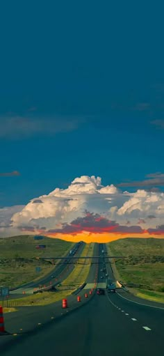 the sun is setting on an empty highway with traffic cones in front of it and clouds above