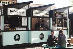 two people sitting at a table in front of a food truck with the door open