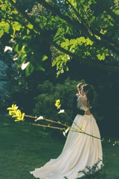 a bride and groom standing under a tree in their wedding gowns, embracing each other