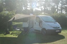 a white van parked in the grass next to a tent and picnic table with chairs