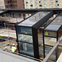 two men are standing on the roof of a building with glass walls and steel bars